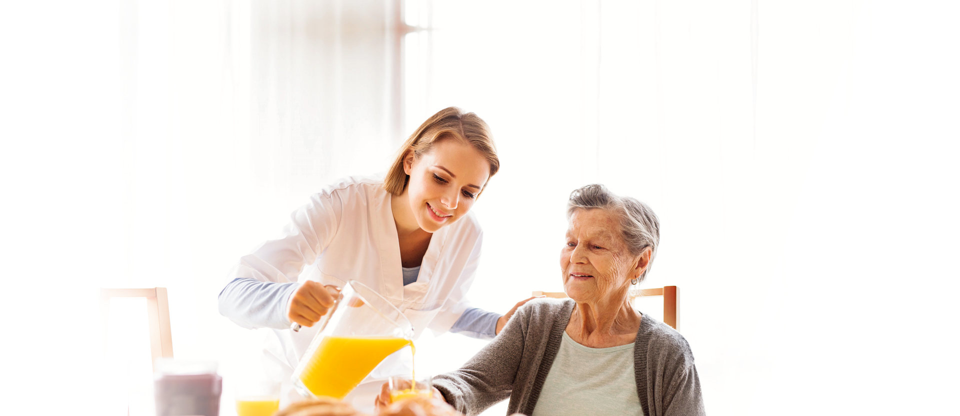 caregiver pouring orange juice to a senior woman's glass